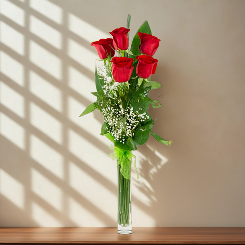 Ramo de rosas rojas en jarrón de vidrio alto Seis rosas rojas con follaje verde y flores blancas pequeñas en un jarrón de vidrio alto y estrecho sobre una repisa de madera