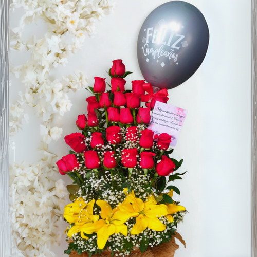 Arreglo floral de rosas rojas y lirios amarillos con globo de feliz cumpleaños Arreglo de flores con varias filas de rosas rojas, lirios amarillos en la base, follaje verde, nube blanca decorativa y globo negro con texto Feliz Cumpleaños