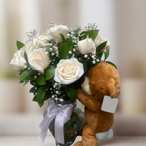 Ramo de rosas blancas y flores pequeñas en jarrón de cristal con lazo blanco acompañado de oso de peluche marrón