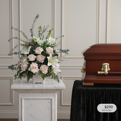 Arreglo de rosas y lirios blancos sobre pedestal de mármol al lado de un ataúd de madera barnizada con herrajes dorados en sala de velatorio
