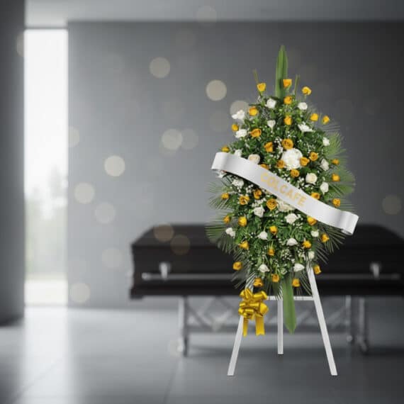 Pedestal fúnebre con rosas amarillas y blancas, follaje verde, y cinta blanca con el nombre 'COLCAFE', en una sala de velació
